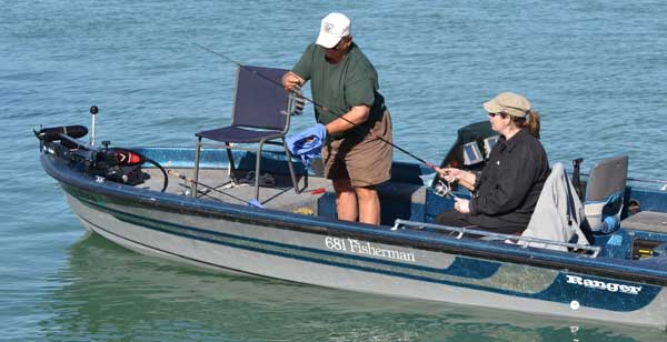 man holding small sheepshead fish on a boat in a bay with a woman watching