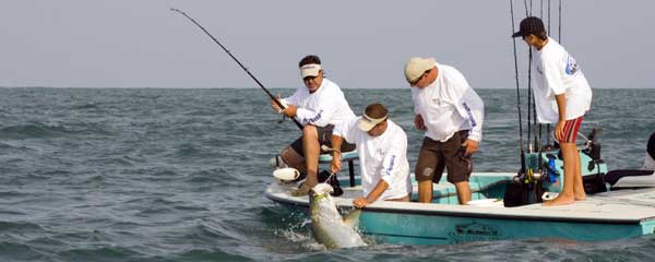 men on a boat with a tarpon fish in the water